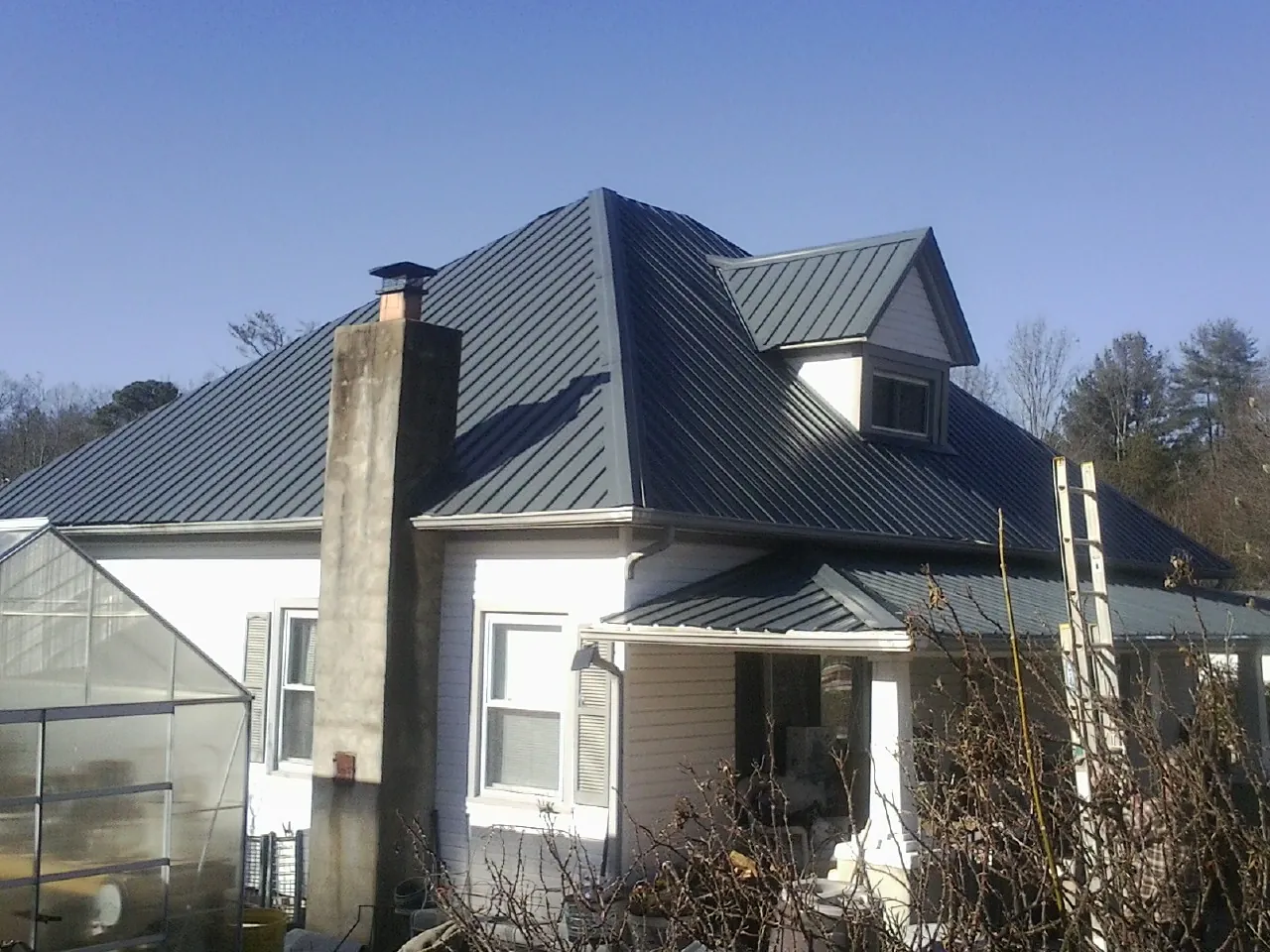 Dark blue standing seam metal roof on a white farmhouse with dormer — Slate & Tile Roof Repair by Roofing Brothers in Medford